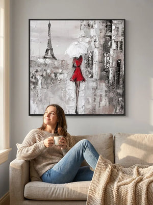 Woman sitting on a couch holding a mug, looking at a large abstract painting of a woman in a red dress with the Eiffel Tower.